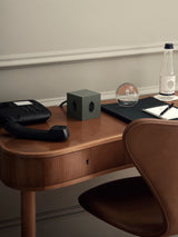 AVOLT Square 1 Swiss edition power extender in dark green on a wooden desk with a phone and stationery.