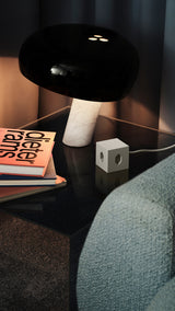 AVOLT Square 1 USB-C (Swiss) sand cube power adapter on glass side table by lamp and books