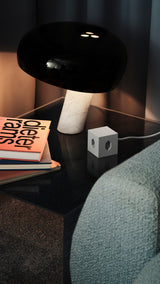 AVOLT Square 1 USB-C (Swiss) power cube on glass side table beside lamp and stacked books