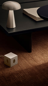 AVOLT Square 1 USB-C (Swiss) beige power cube on carpet beside coffee table and lamp