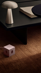 AVOLT Square 1 USB-C (Swiss) cube charger, soft pink on carpet beside a low black table