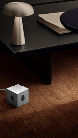 AVOLT Square 1 USB-C (Swiss) power cube on brown carpet beside low table and mushroom lamp