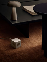 Beige AVOLT Square 1 USB-C power cube with EU outlets on carpet beside black coffee table and lamp