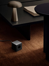 AVOLT Square 1 USB-C power cube on brown carpet beside low black table and brass lamp