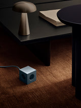 lifestyle: AVOLT Square 1 - USB-C blue cube power outlet on carpet beside low table, visible cable