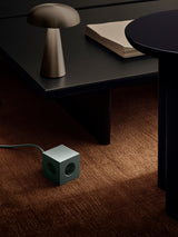 AVOLT Square 1 - USB-C green power cube on carpet beside low table and mushroom lamp