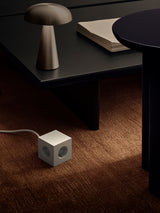 Grey AVOLT Square 1 USB-C power cube on carpet beside low coffee table and lamp