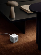 AVOLT Square 1 USB-C power cube on carpet beside low black table and brass mushroom lamp