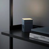 AVOLT Lamp 1 Shark Blue på skrivebordshylde, varmt toplys ved siden af bøger og en lukket laptop