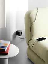 AVOLT Square 2 USB-C power cube plugged into wall charging phone with cable draped over sofa