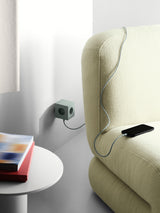 AVOLT Square 2 USB-C power cube mounted on wall charging phone on sofa, green cube with grey cable