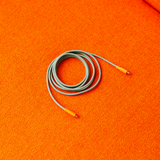 AVOLT Cable 1 - Bauhaus-Archiv - Gecko Bloom USB-C cable τυλιγμένο, πράσινο φασκόμηλο με κοραλλί άκρα σε πορτοκαλί ανάγλυφη επιφάνεια.