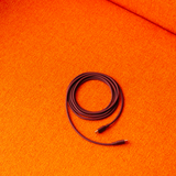 AVOLT Cable 1 - Bauhaus-Archiv - Mulberry Red USB-C cable, τυλιγμένο σε μια ζωντανή, πορτοκαλί, ανάγλυφη επιφάνεια.