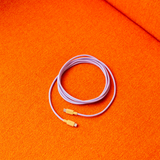 AVOLT Cable 1 - Bauhaus-Archiv - USB-C σε USB-C 2μ. Lavender Glow, περιτυλιγμένο σε πορτοκαλί επιφάνεια.